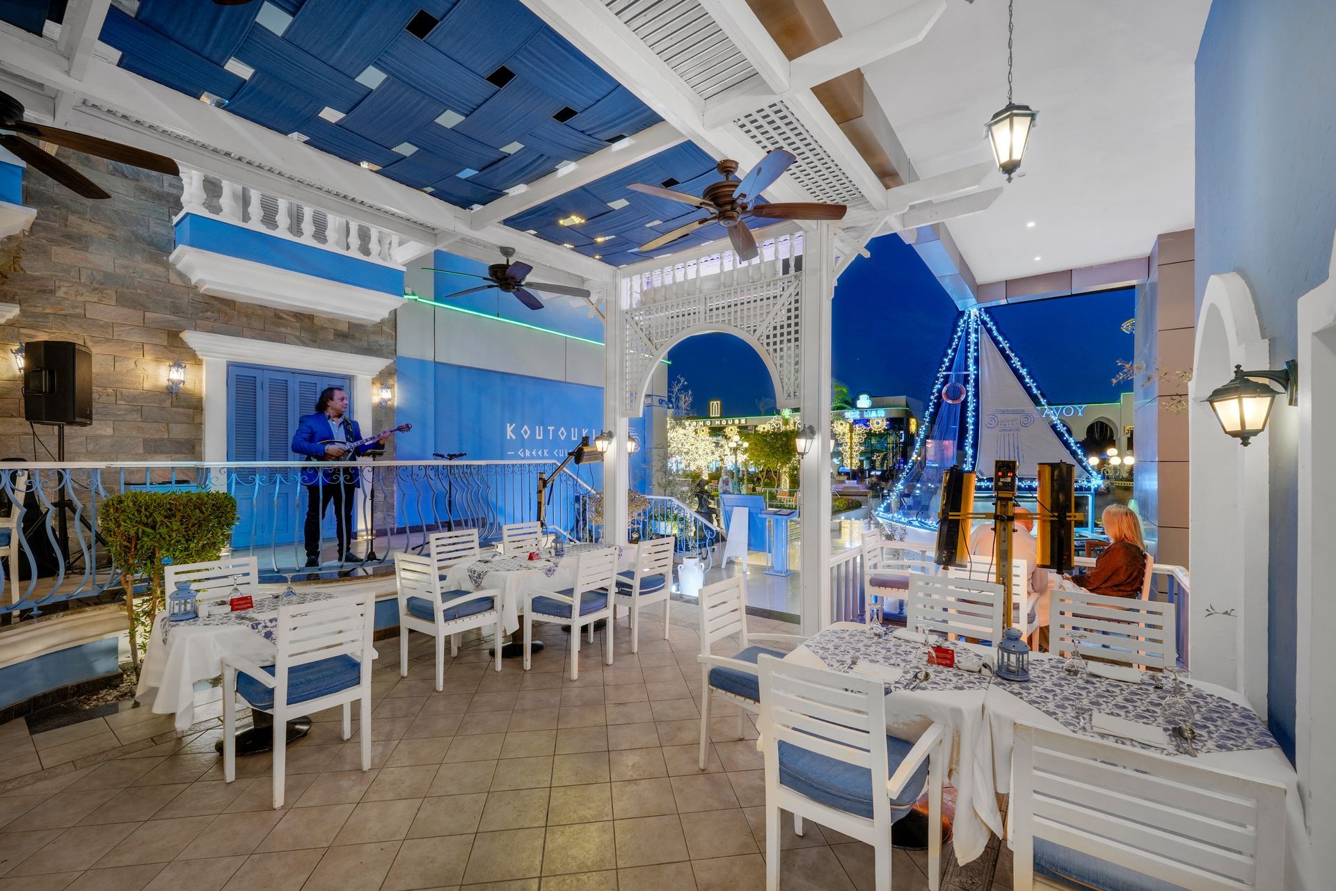 Restaurant patio with blue and white decor, a performer on stage, and tables set for dining.