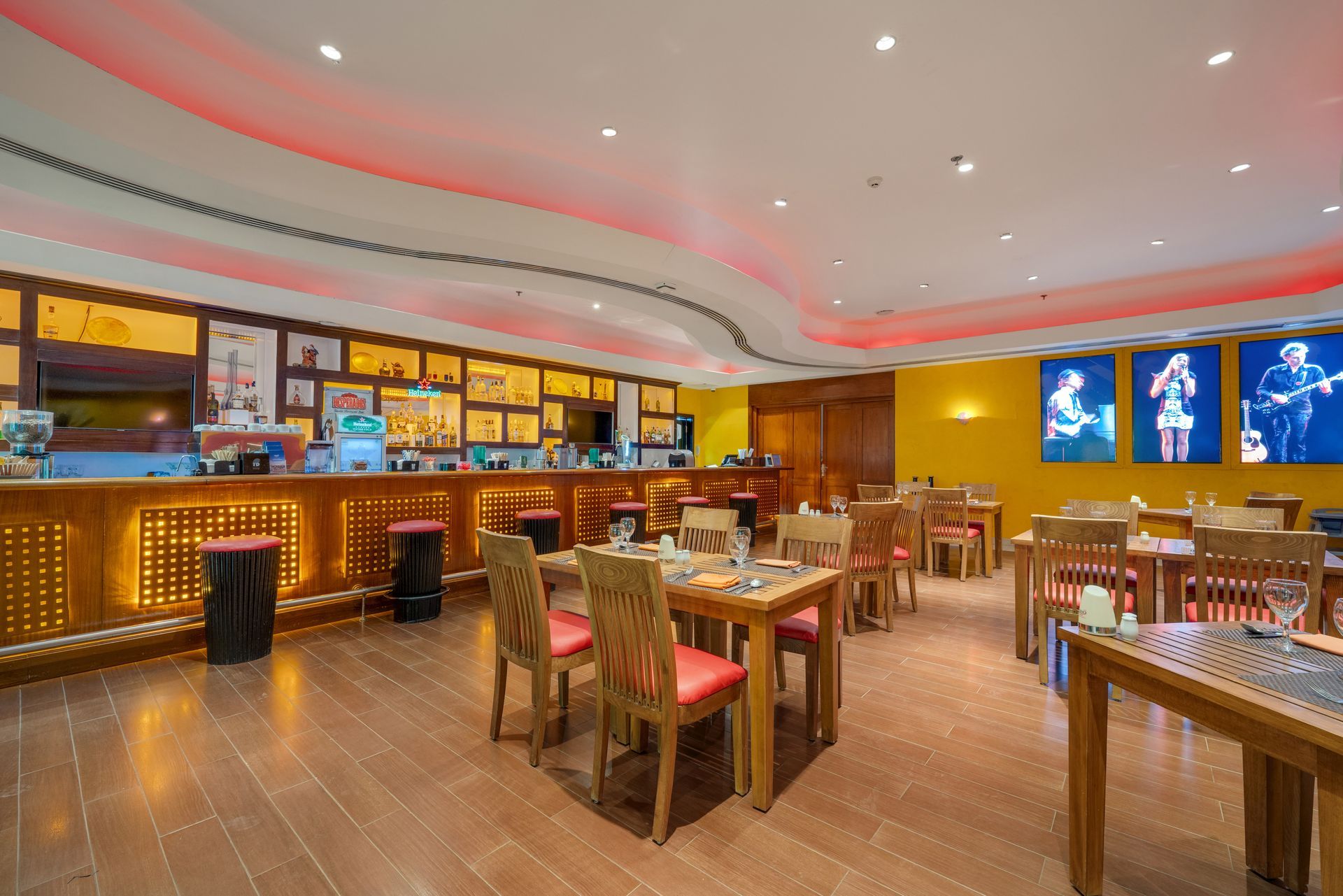 Restaurant interior with tables, chairs, and a bar. Walls are yellow, and there are photos of musicians.