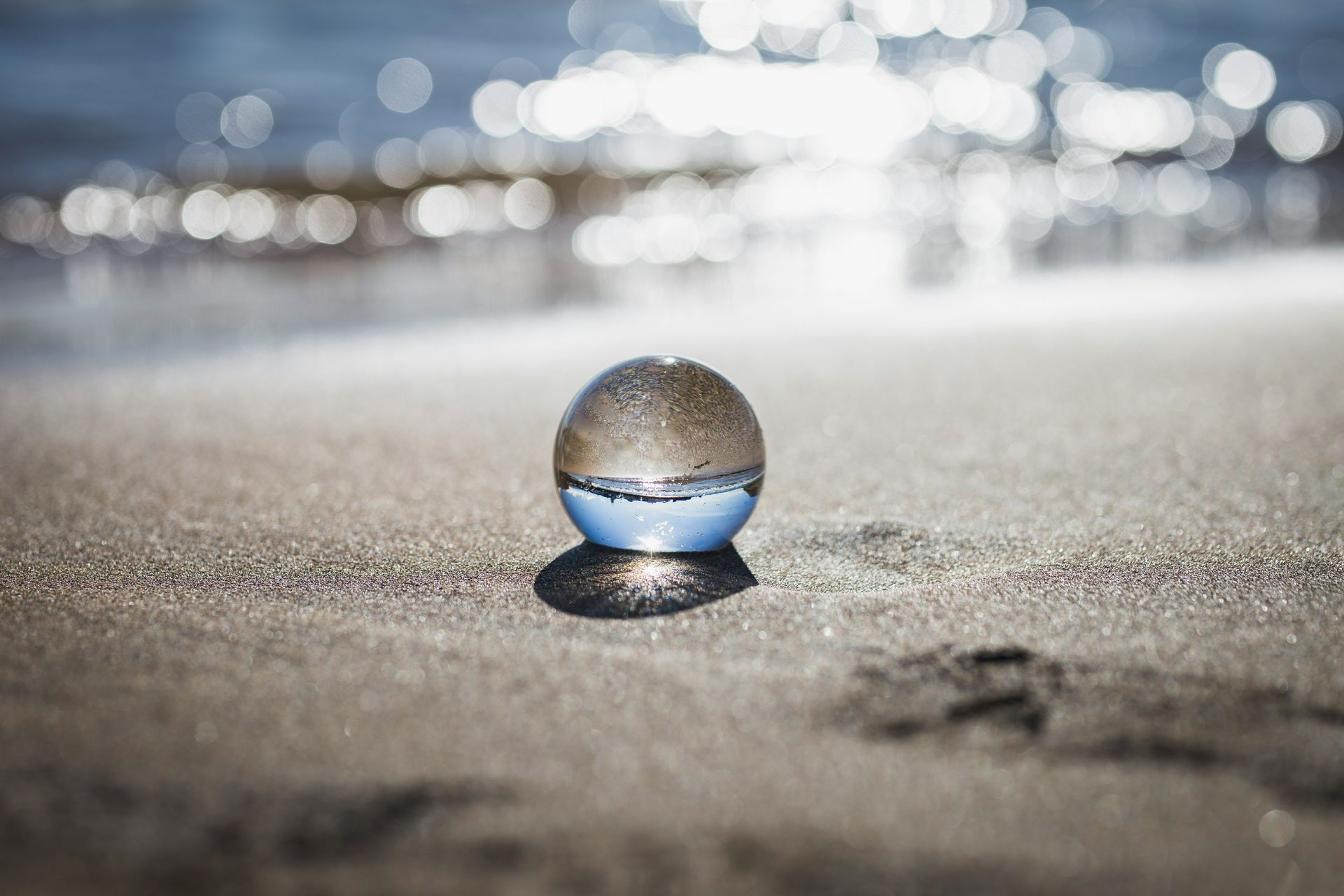 A glass ball is sitting on the beach near the water.