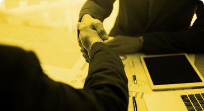 Two people are shaking hands in front of a laptop computer.