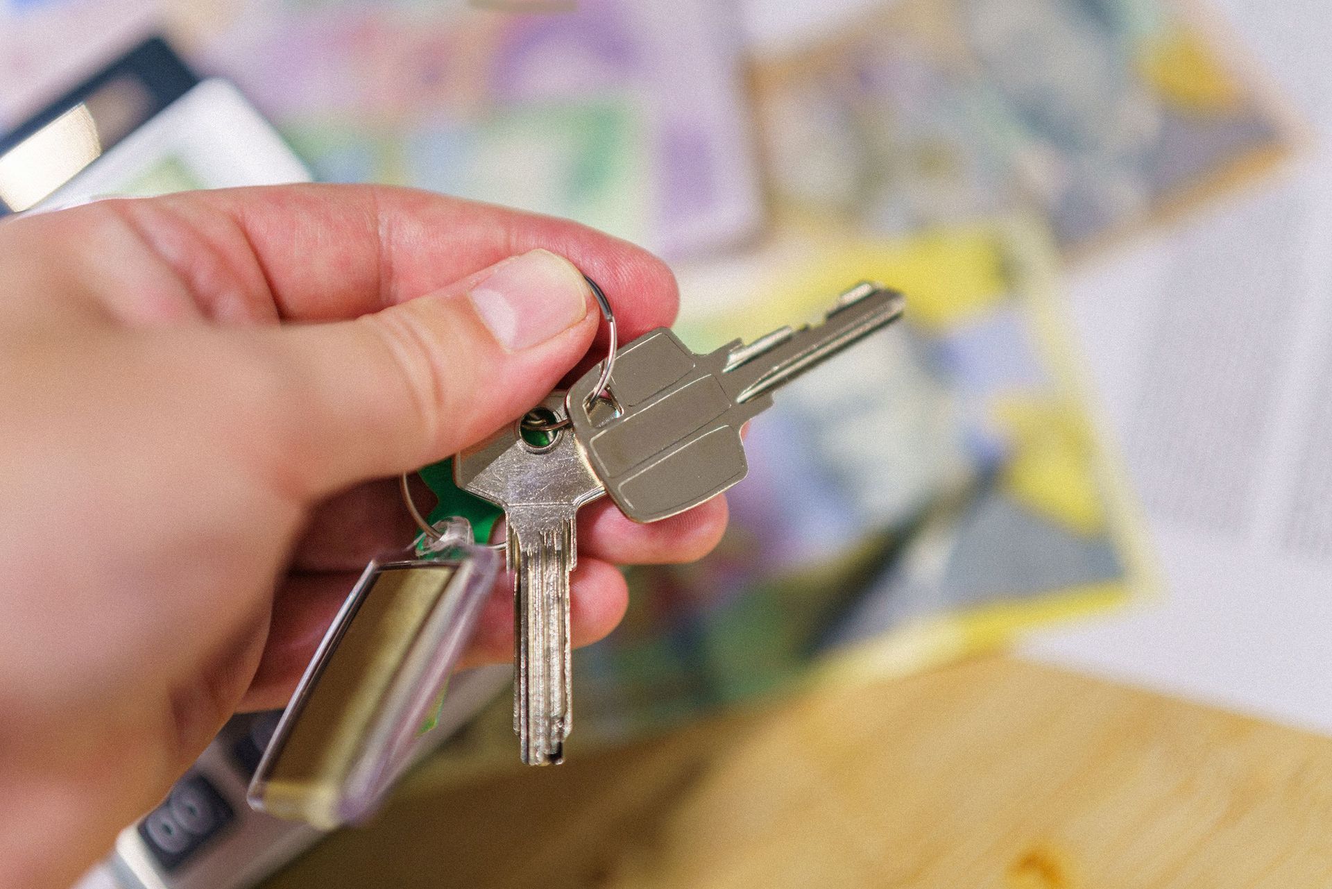 Hand holding a key ring with several metal keys against a blurred indoor background
