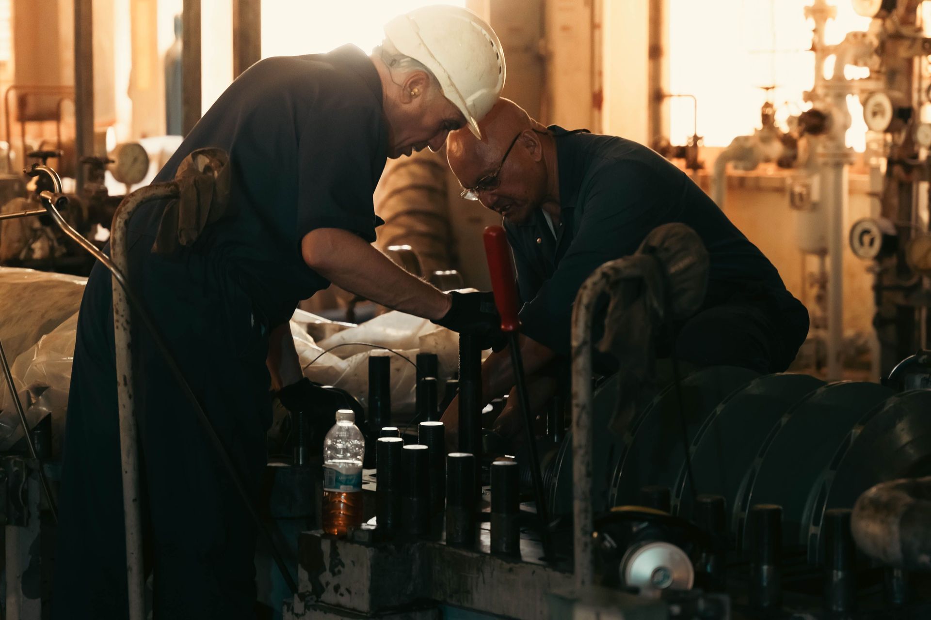 Two workers in a workshop inspecting equipment beside a large machine, with warm industrial lighting