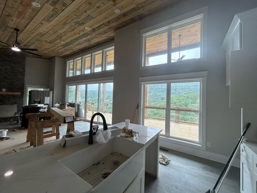Modern kitchen with vaulted wood ceiling, large windows, white island sink, and black faucet