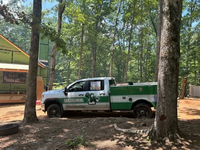 White and green utility truck parked among trees in a wooded area near a building