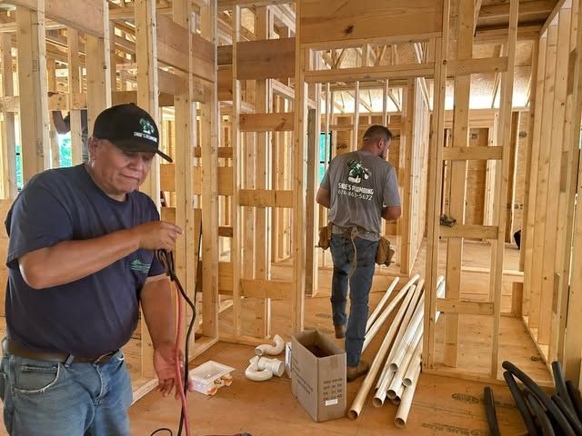 Construction workers framing a house interior with exposed wooden studs and stacked lumber.