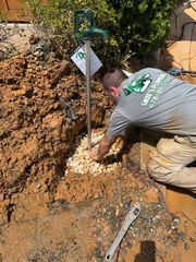 Worker kneeling in dirt beside a metal pipe, digging at a construction site.