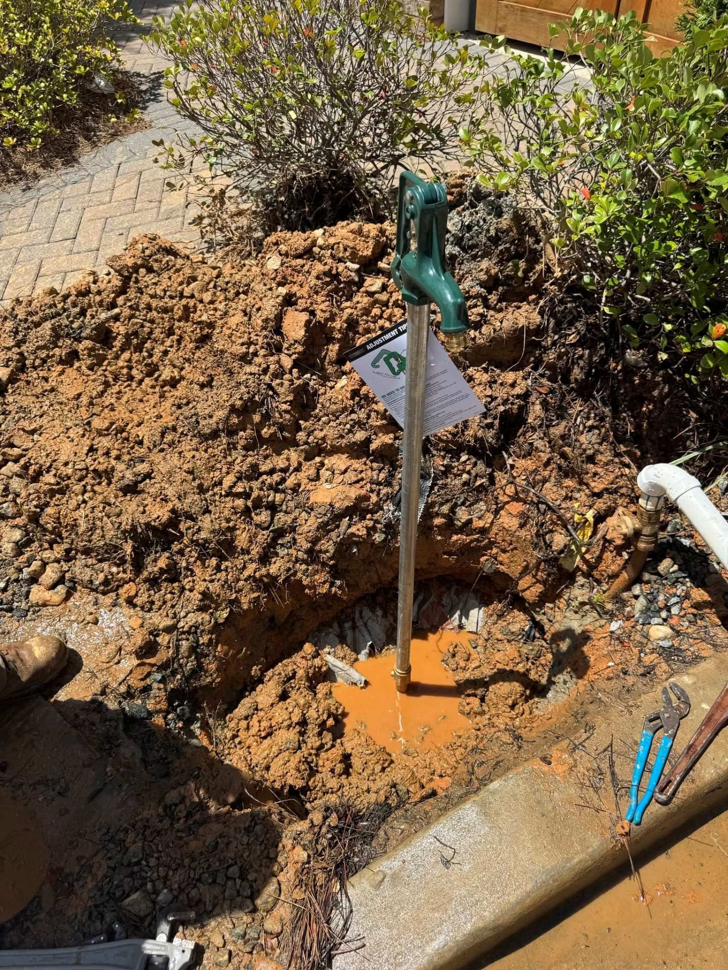 Digging tool in a dirt trench beside a garden path, with orange muddy water around the post.