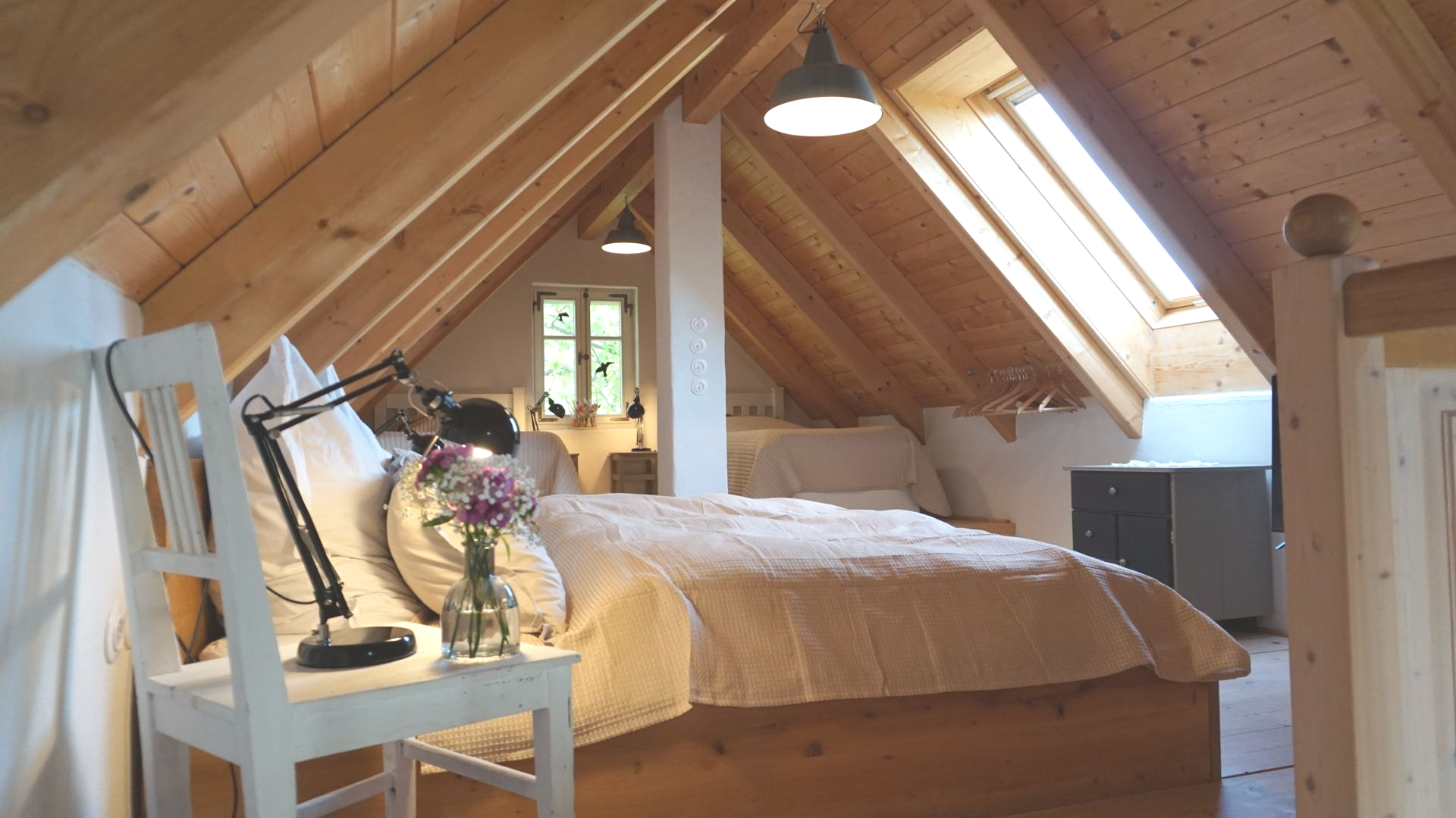 Schlafzimmer im Dachgeschoss mit hellen Holzbalken und einem Bett mit heller Decke.