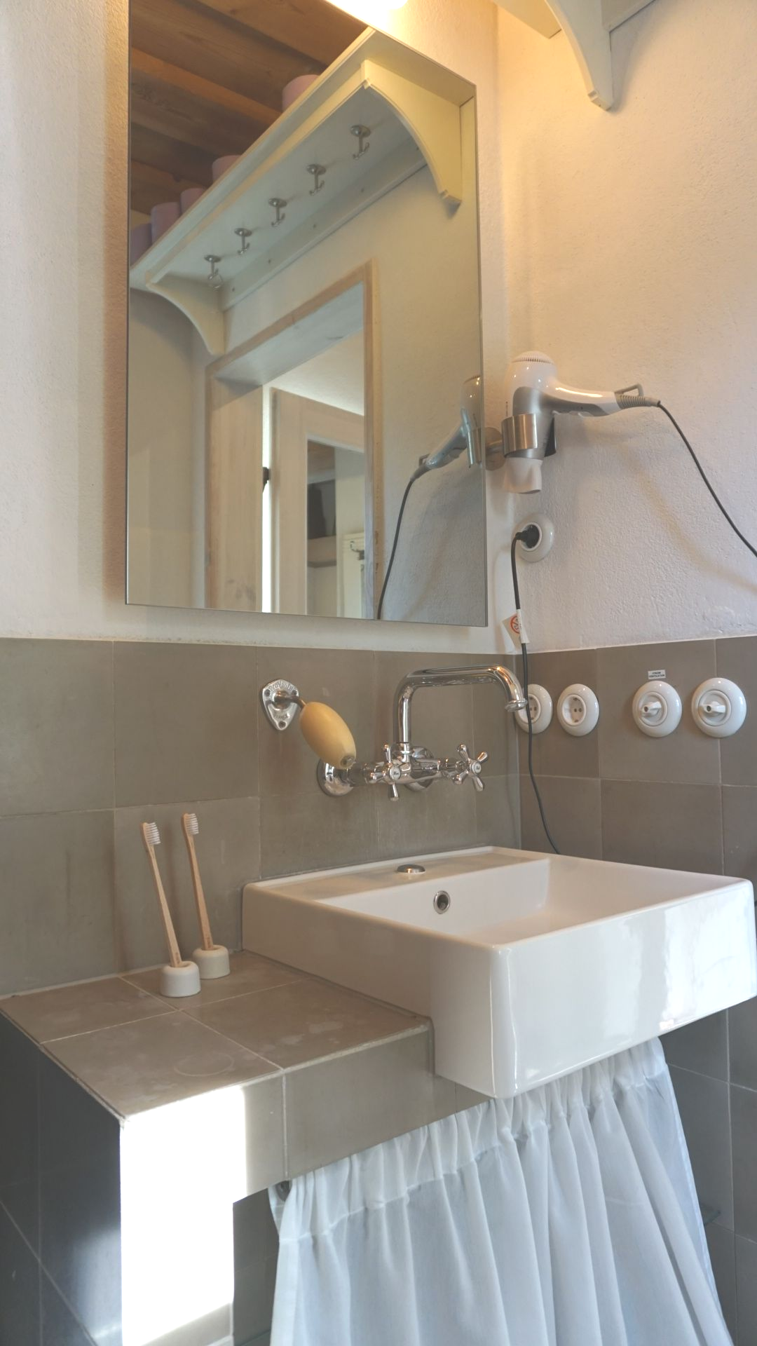 Badezimmer mit quadratischem Waschbecken, Spiegel, Haartrockner und Zahnbürstenhaltern.