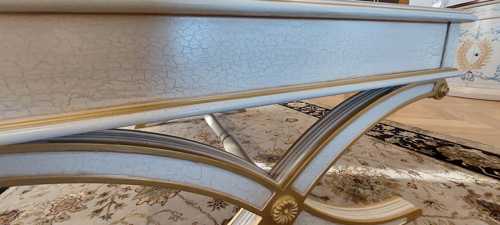 A white and gold table is sitting on a wooden floor.