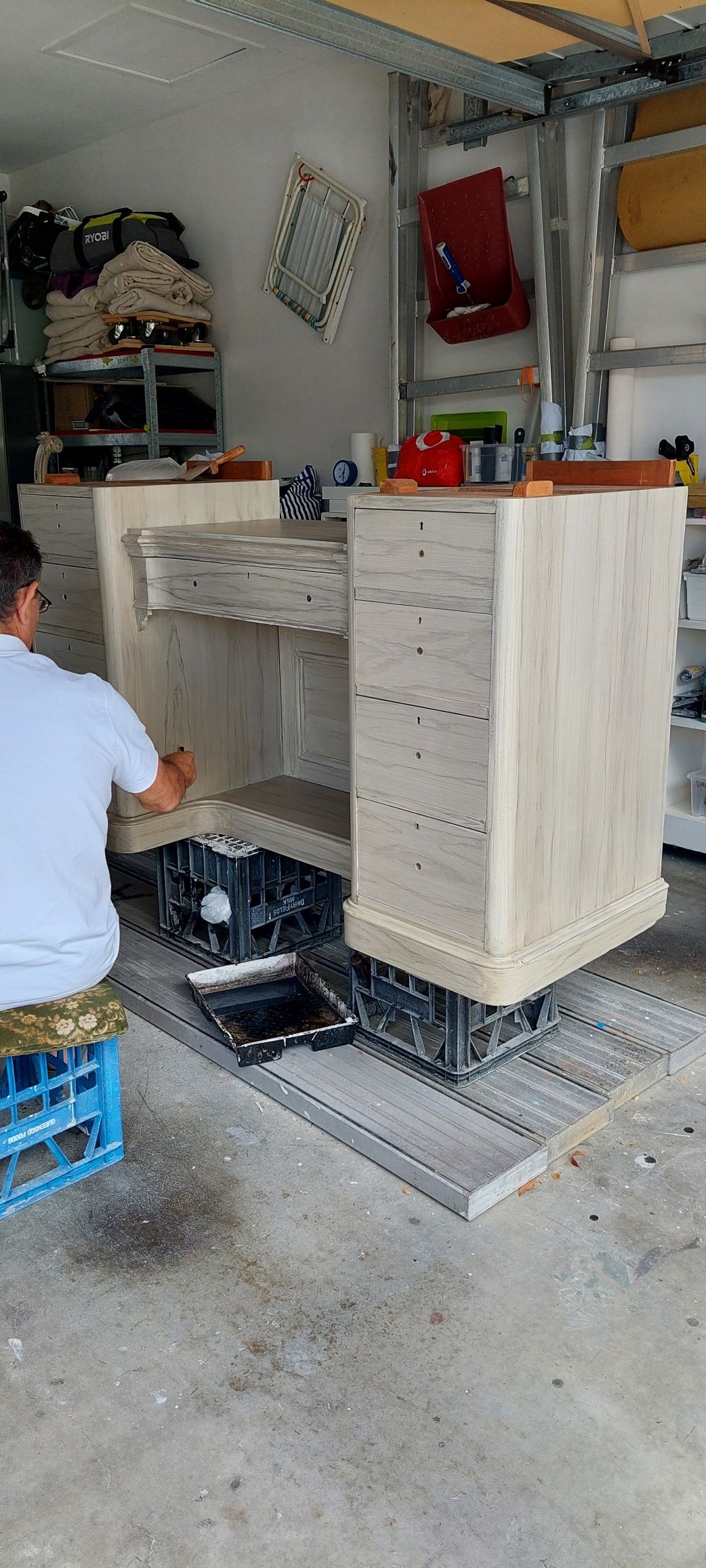 A man is painting a dresser in a garage.