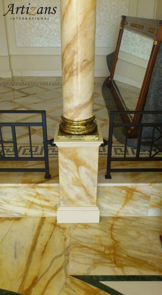 A marble column is sitting on top of a marble floor next to a mirror.