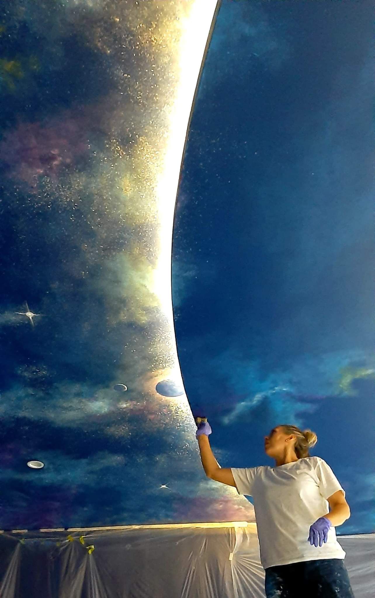 A woman is painting a picture of the moon on a wall.