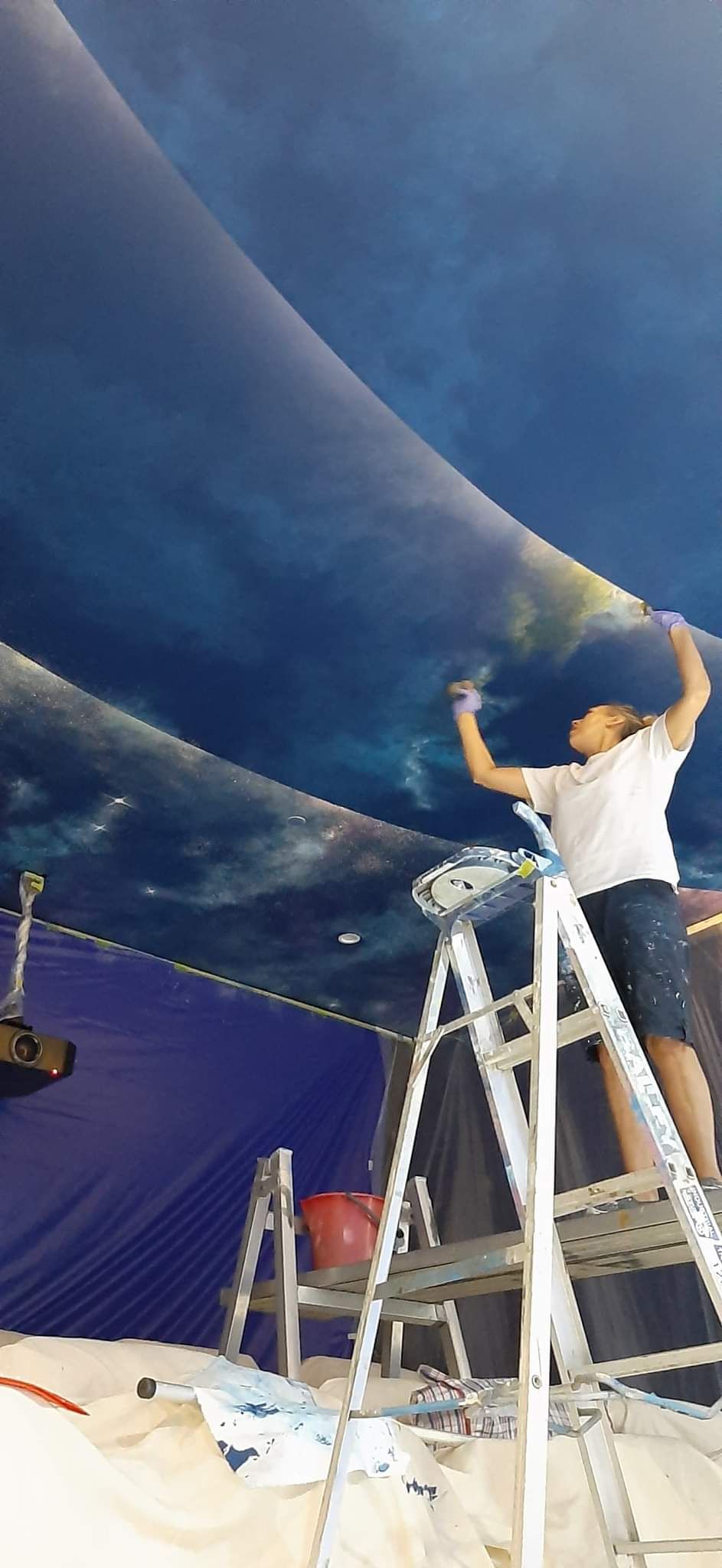 A man is standing on a ladder painting a ceiling.