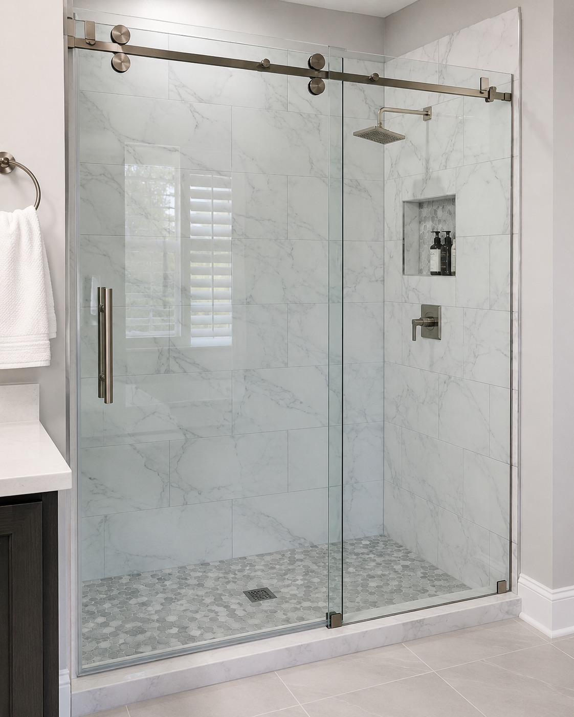 Glass walk-in shower with marble tile walls and pebble floor in a bright bathroom