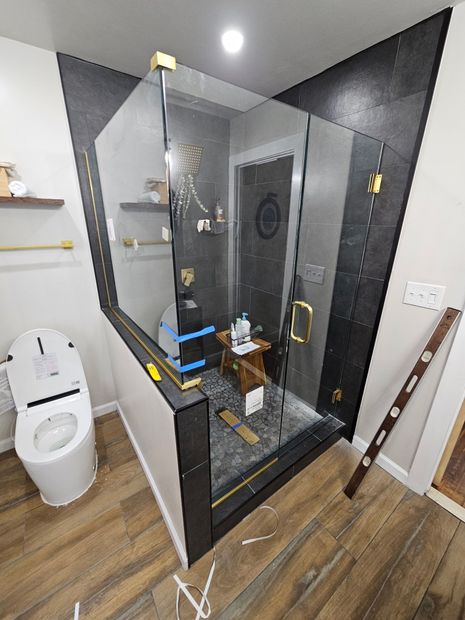 Frameless corner shower enclosure with brushed gold hardware and dark tile