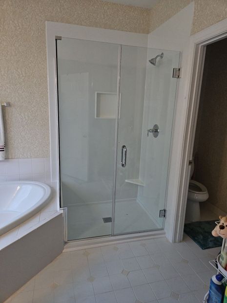 Frameless hinged shower door with inline panel and chrome hardware in an alcove