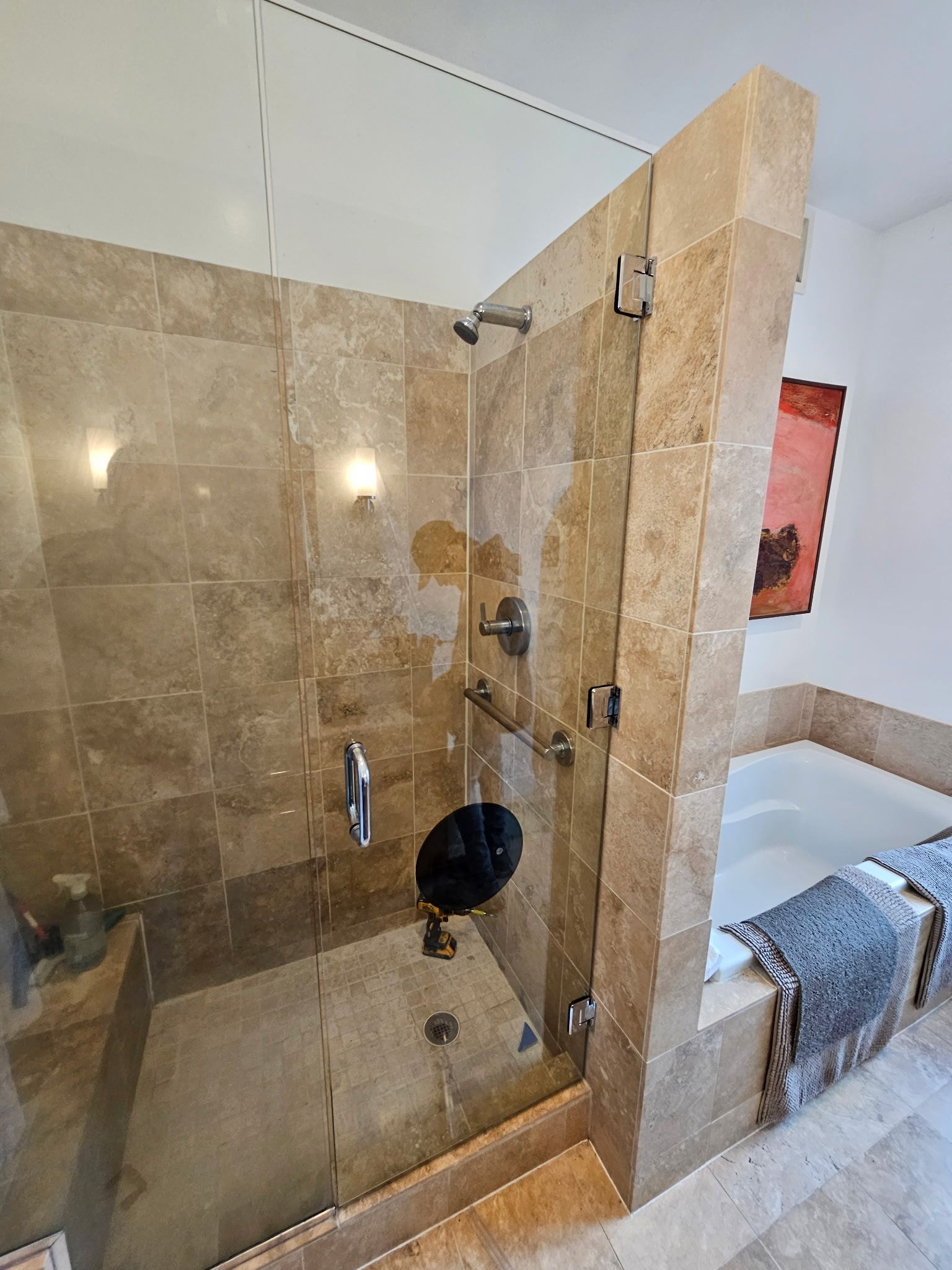 Frameless glass shower door with black hardware over dark tile, installed by Baltimore Glass Company