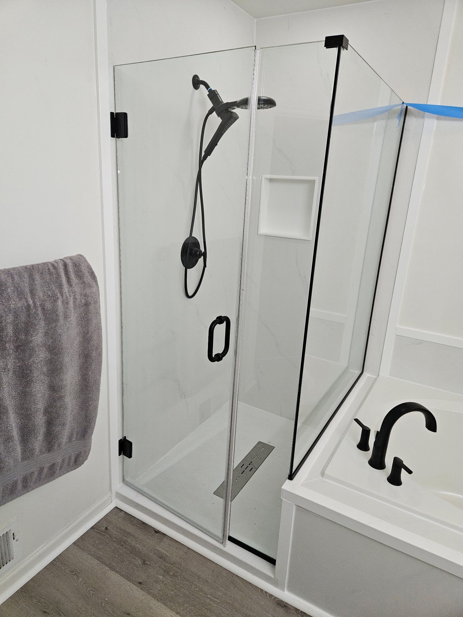 Frameless hinged shower door with return panel, matte black hardware, and linear drain in Baltimore, MD