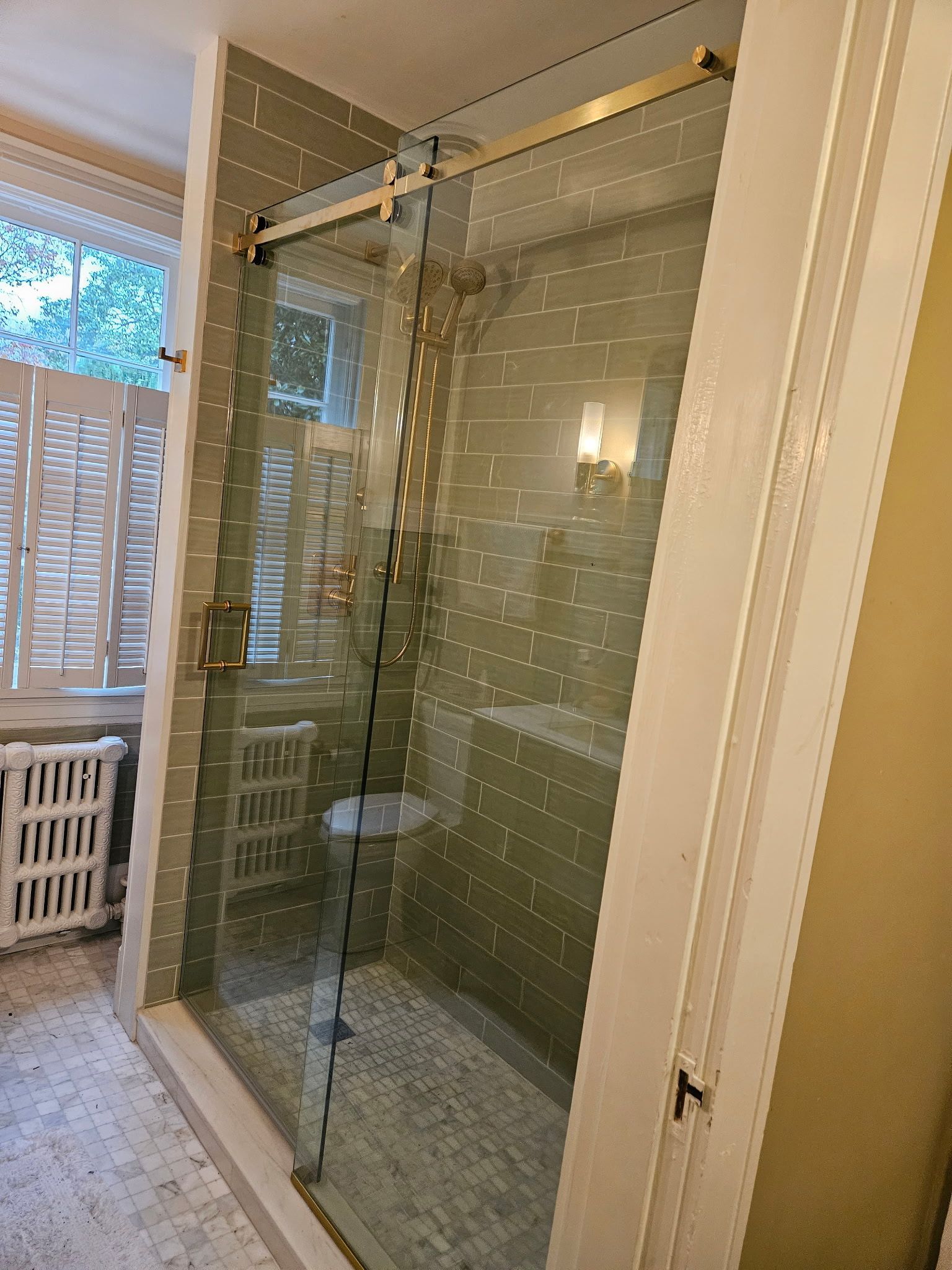 Sliding shower door with brushed brass rollers and green subway tile in Baltimore, MD