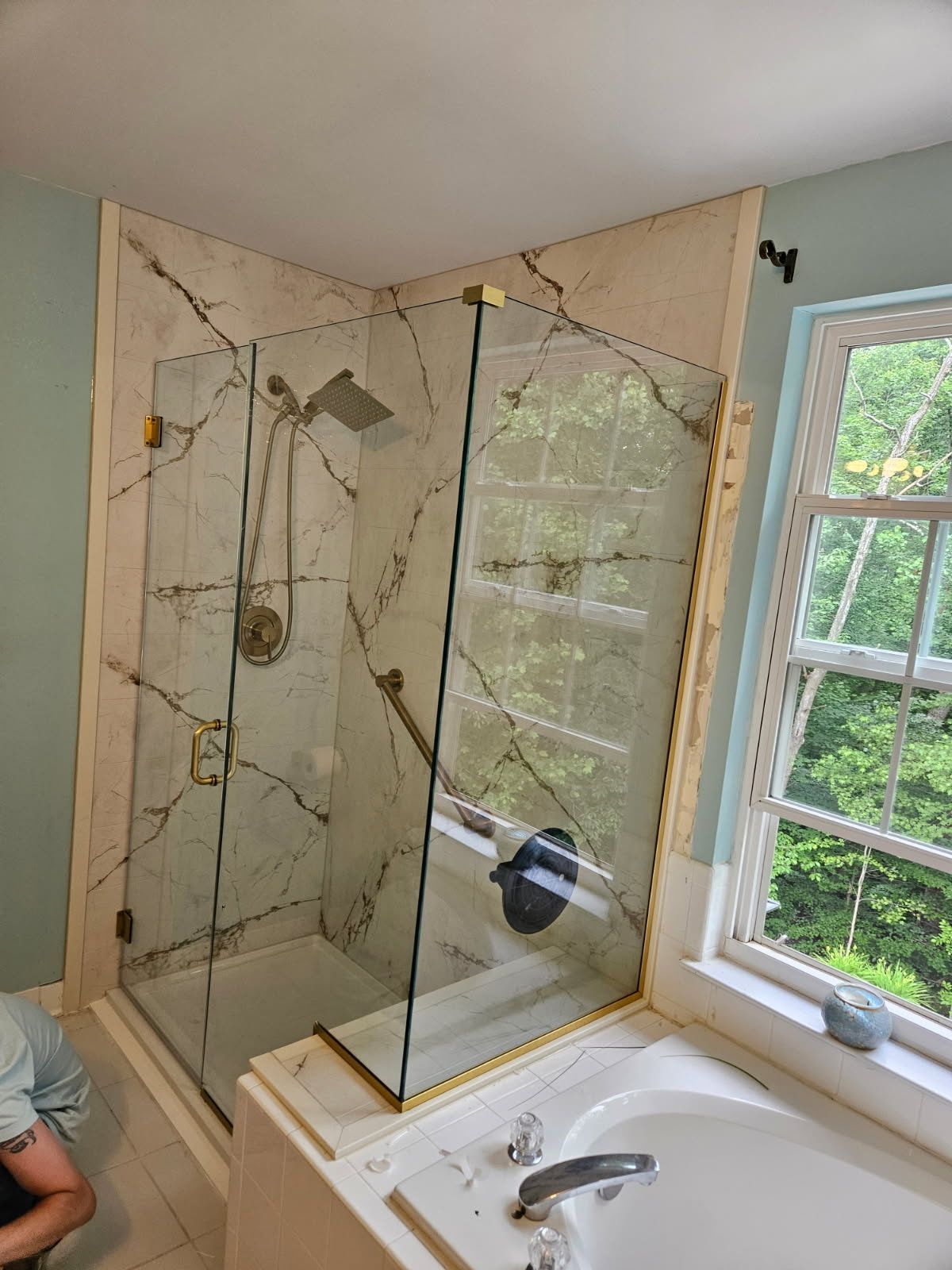 Frameless corner shower enclosure with brass hardware and marble tile installed in Baltimore, MD