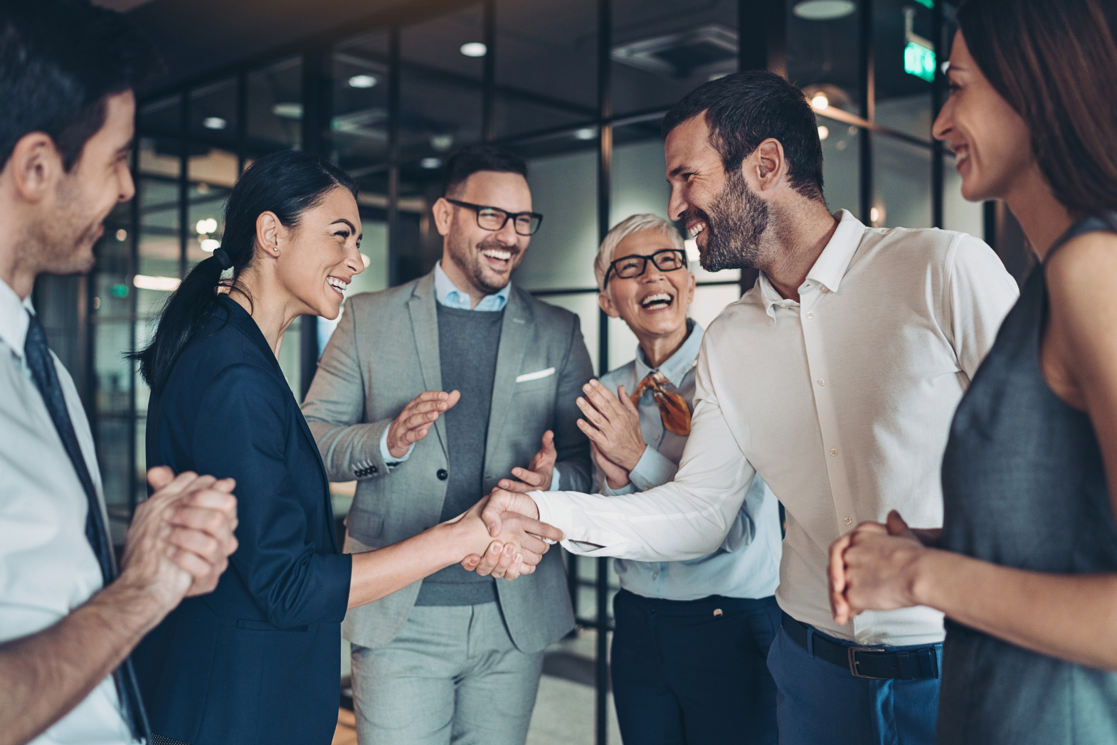 A group of professional colleagues in a modern office, smiling as they shake hands to celebrate a successful collaboration.