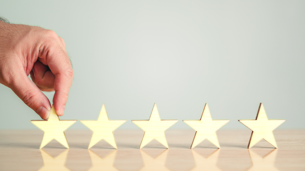 A hand places a gold star into a row of five stars on a wooden surface against a light gray background.