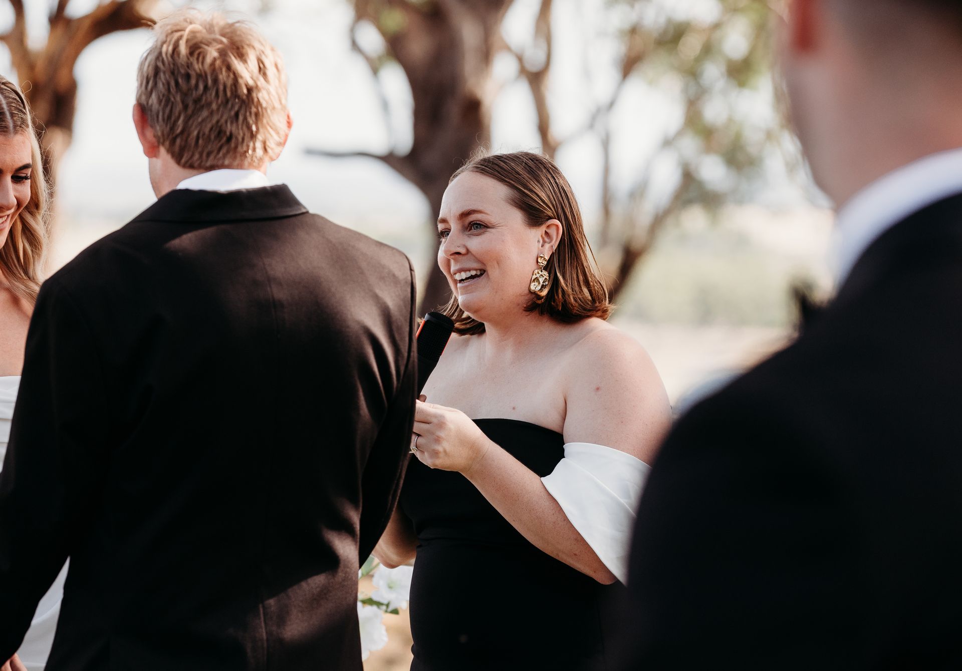 Smiling woman in a black dress talking outdoors at a wedding gathering