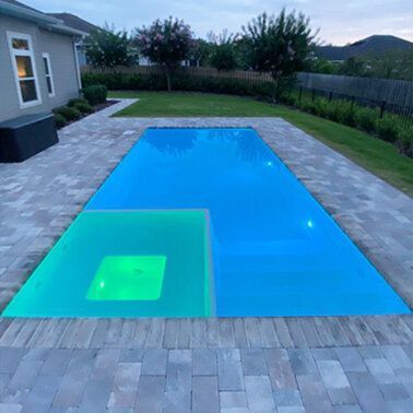 A large swimming pool is surrounded by a brick patio and a house.