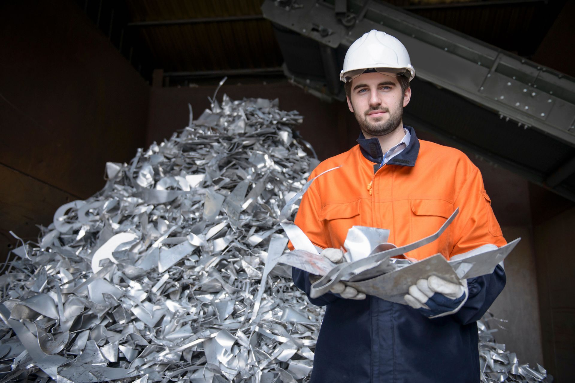 Construction worker in safety gear handling metal scraps at industrial recycling scrap yard site.