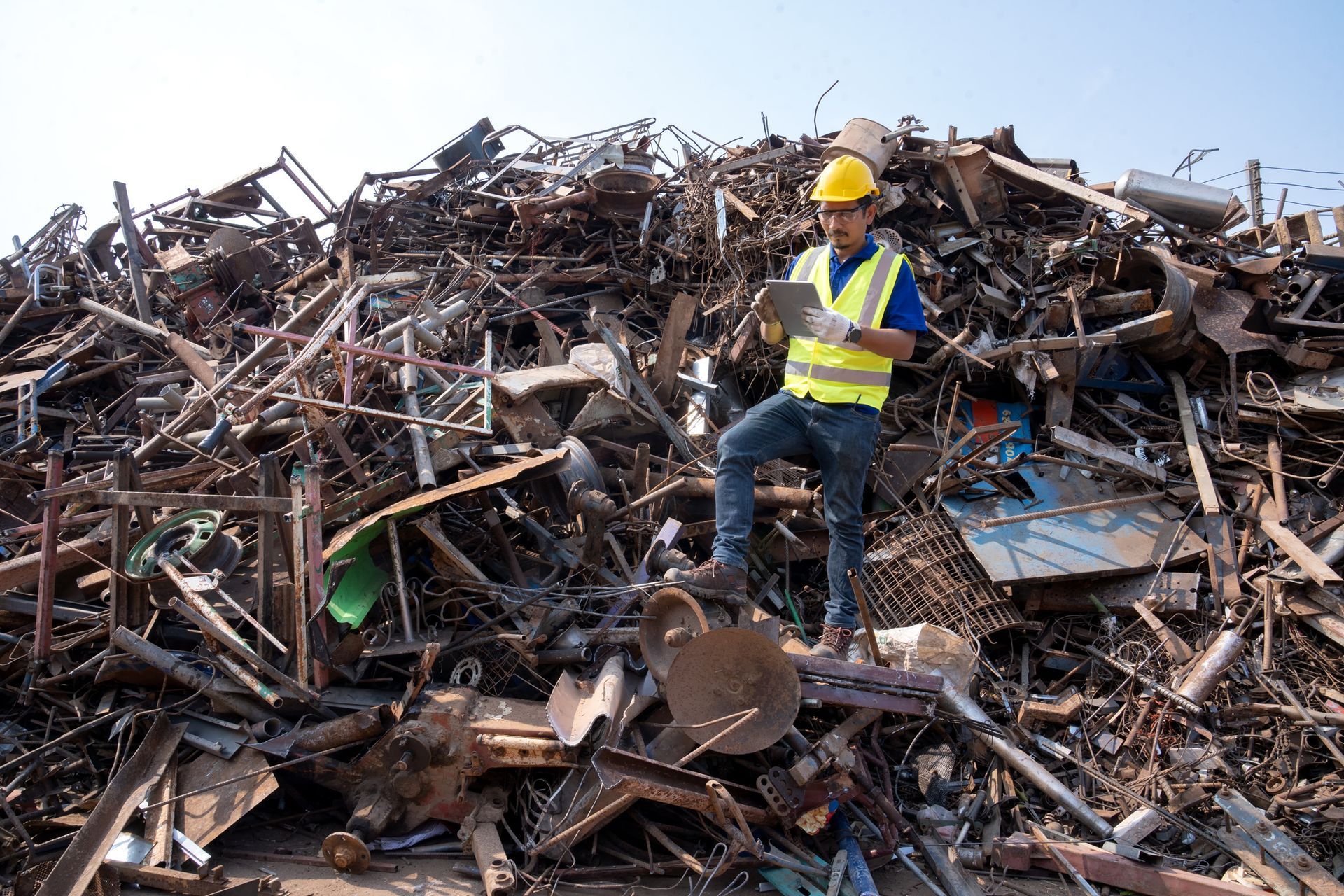 Engineer in safety gear inspecting metal scrap yard with heavy machinery recycling steel scrap.