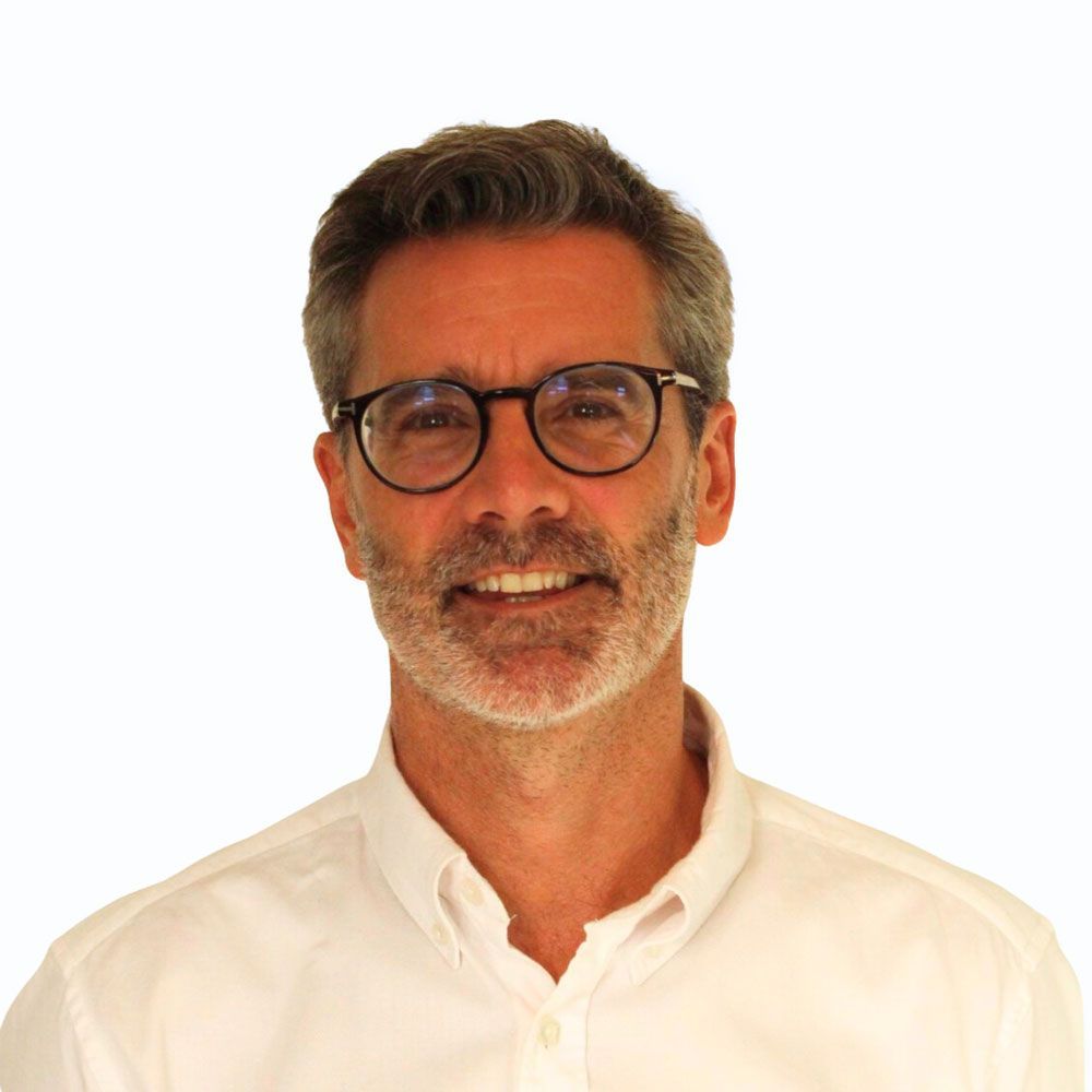 Man with glasses, wearing a striped shirt, smiling in front of a white background.