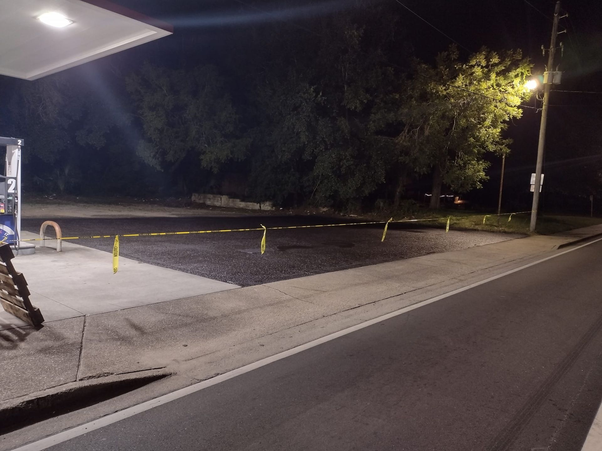 Gas station lot at night, covered in gravel and caution tape.
