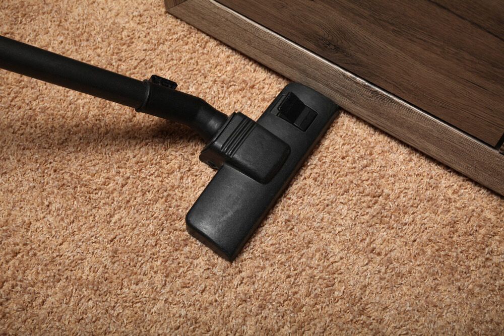 Vacuum Cleaner Head on Beige Carpet Beside a Wooden Cabinet — Broadbeach Carpet Cleaning In Broadbeach, QLD