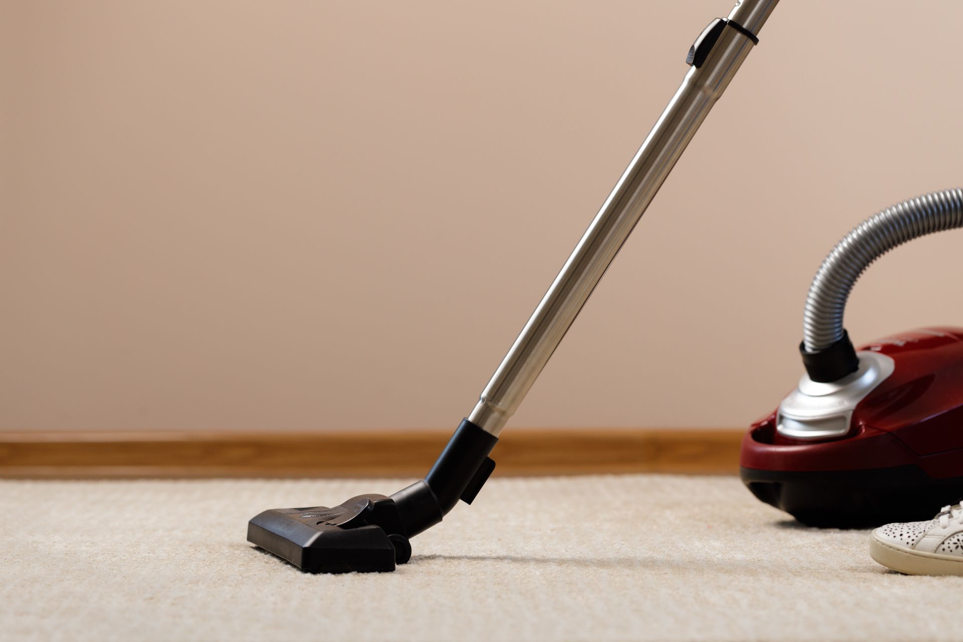 Vacuum cleaner nozzle on beige carpet beside a red canister vacuum — Broadbeach Carpet Cleaning In Mermaid Beach, QLD