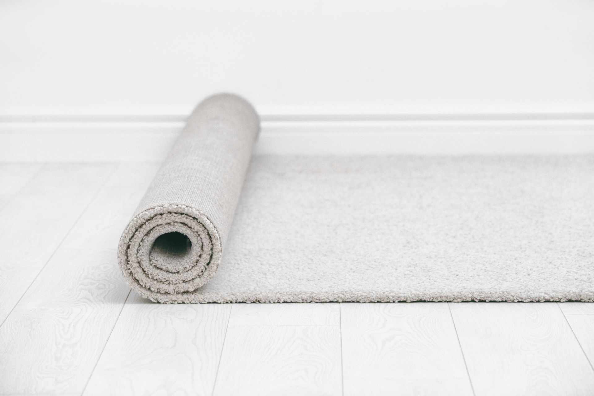 Rolled Gray Rug on A Light Wood Floor Against a White Wall — Broadbeach Carpet Cleaning In Surfers Paradise, QLD