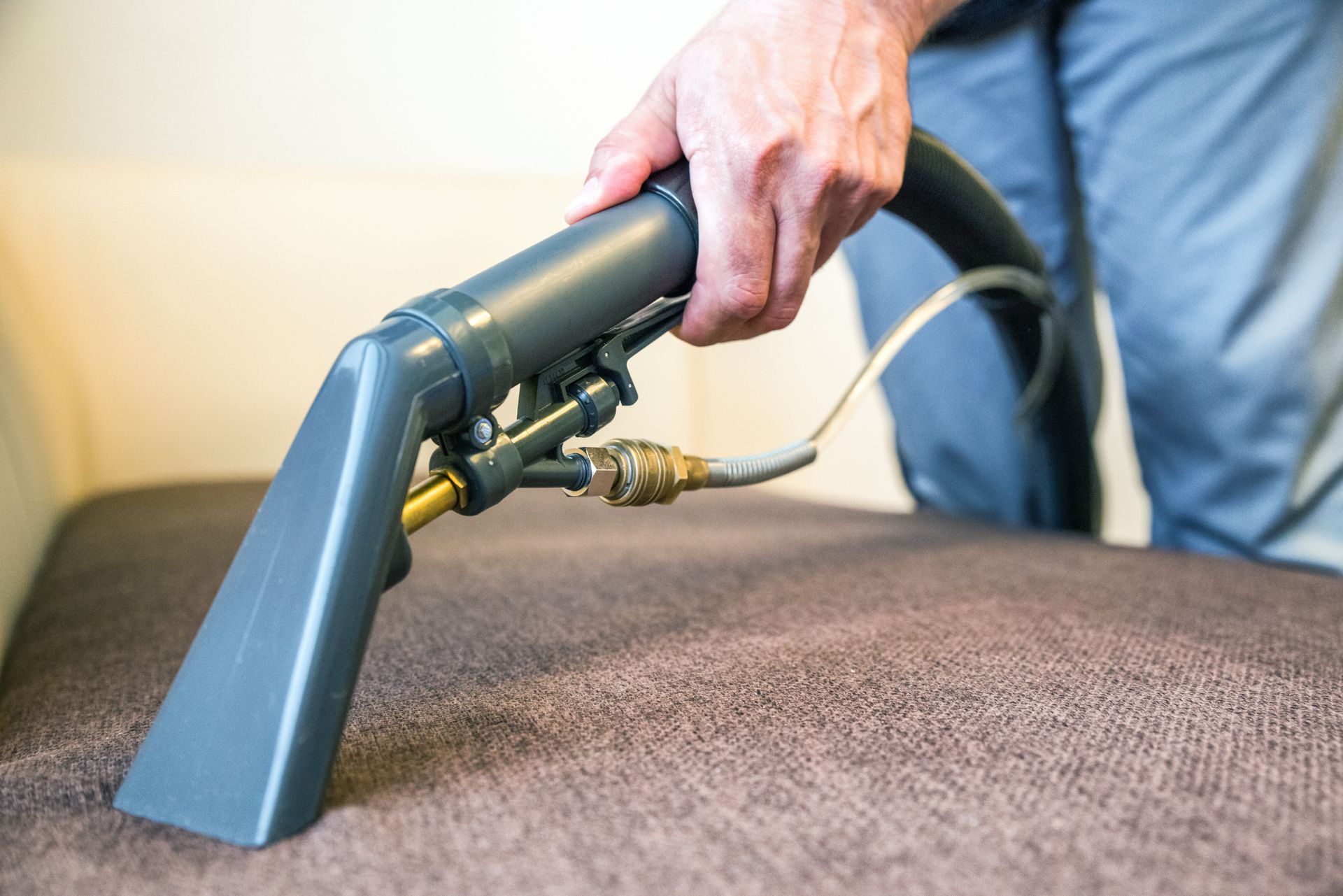 Hand using upholstery vacuum attachment to clean a gray sofa — Broadbeach Carpet Cleaning In Burleigh Heads, QLD