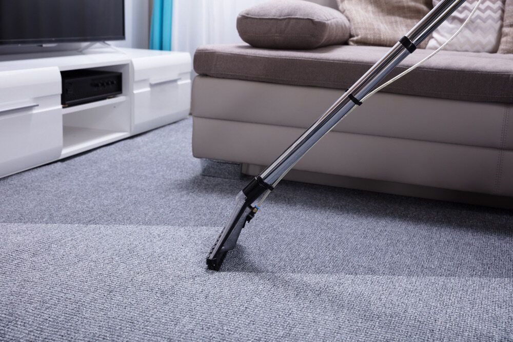 Vacuum Cleaning Gray Carpet Beside a Beige Sofa in A Living Room — Broadbeach Carpet Cleaning In Broadbeach, QLD