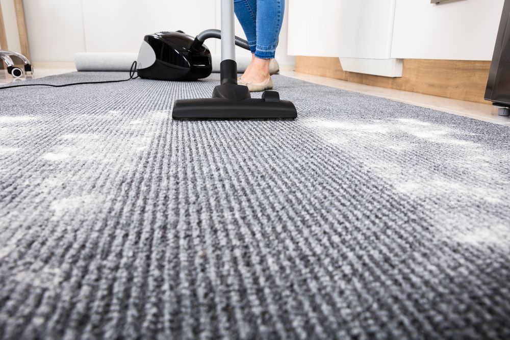 Person Vacuuming a Gray Carpet in A Bright Room — Broadbeach Carpet Cleaning In Broadbeach, QLD
