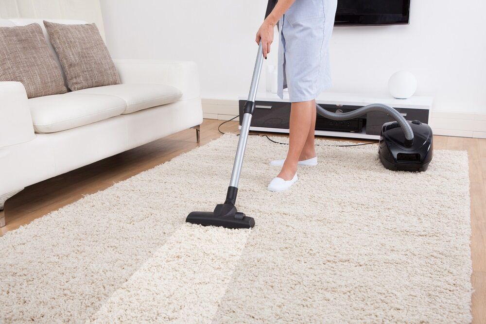Person Vacuuming a White Shag Rug in A Bright Living Room — Broadbeach Carpet Cleaning In Mermaid Beach, QLD
