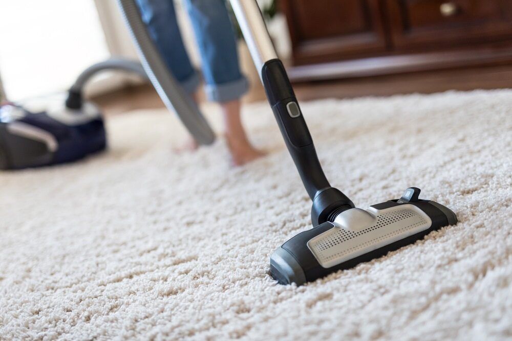 Person Vacuuming a Beige Carpet with A Black Upright Vacuum Cleaner — Broadbeach Carpet Cleaning In Bundall, QLD