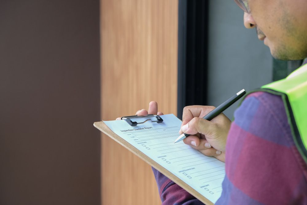 A Man Is Writing on A Clipboard with A Pen — Edwards & Froud Building Services Pty Ltd in Armidale, NSW