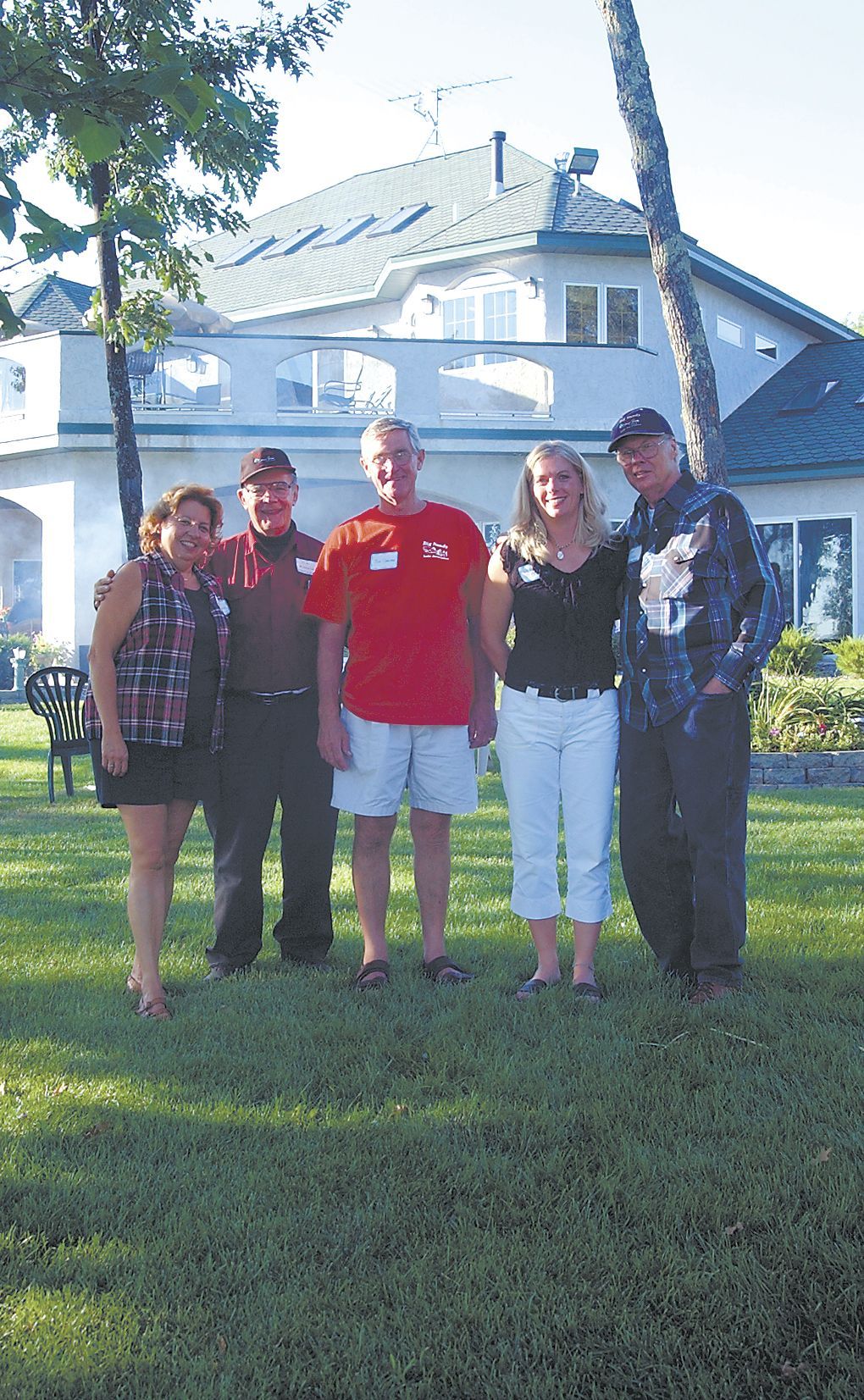 Four people standing on a lawn in front of a white house, smiling in daylight.