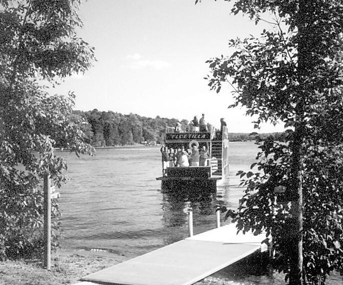 Dock leading to a boat on a lake, framed by trees on both sides.