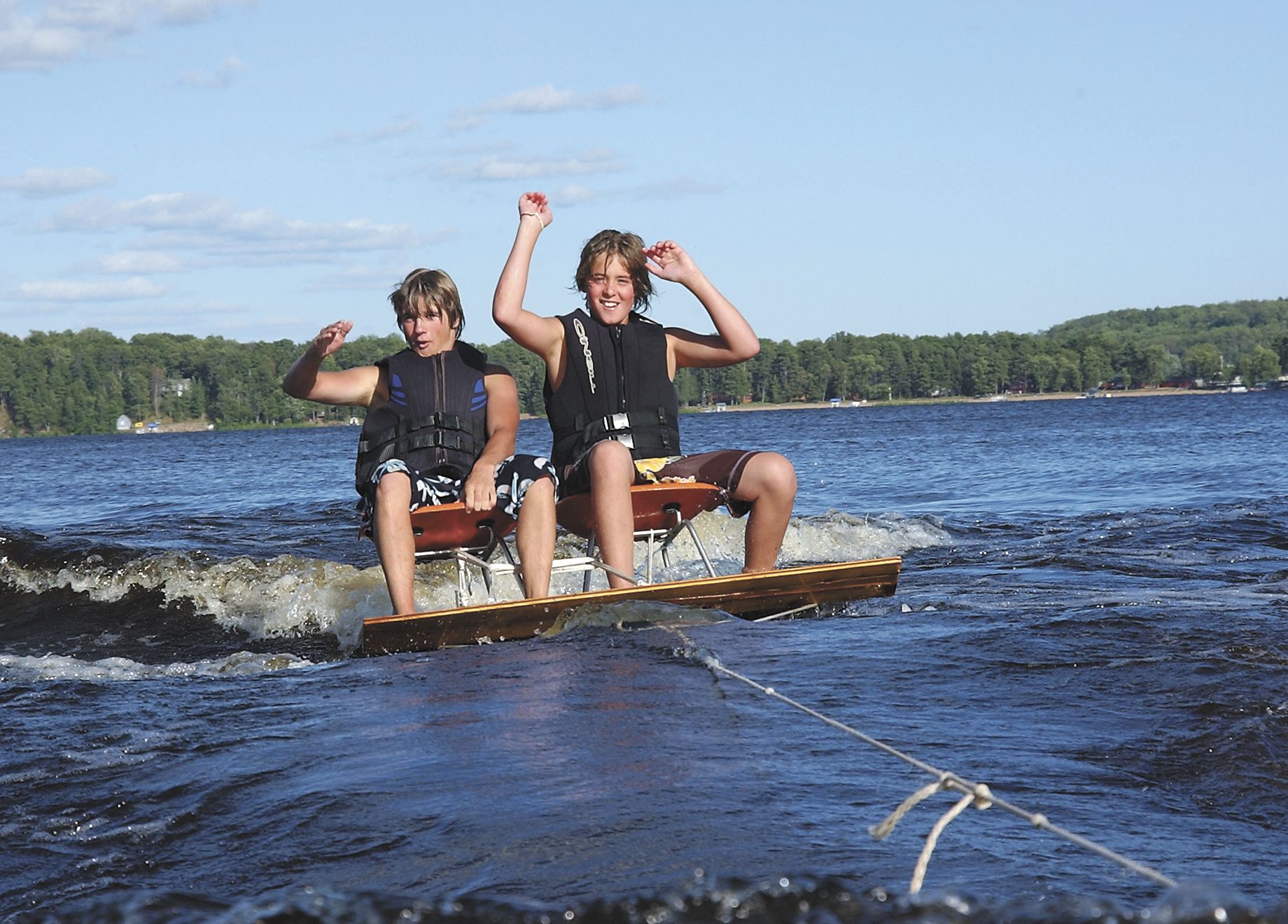 Two people on a small raft on a lake, splashing through the water with raised arms.
