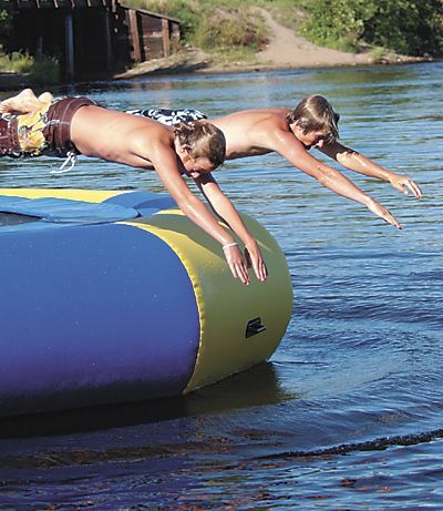 Two people diving off a blue inflatable raft into a river