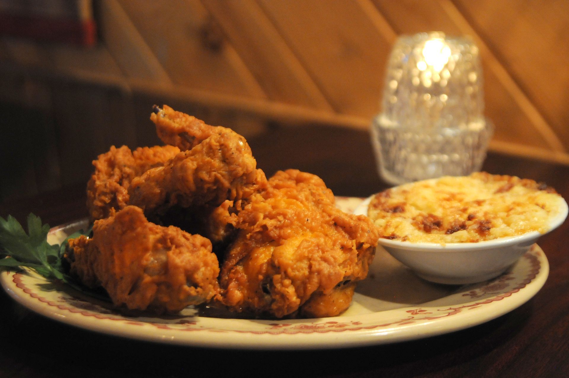 Fried chicken on a plate beside a bowl of mashed potatoes in a warm, rustic dining setting