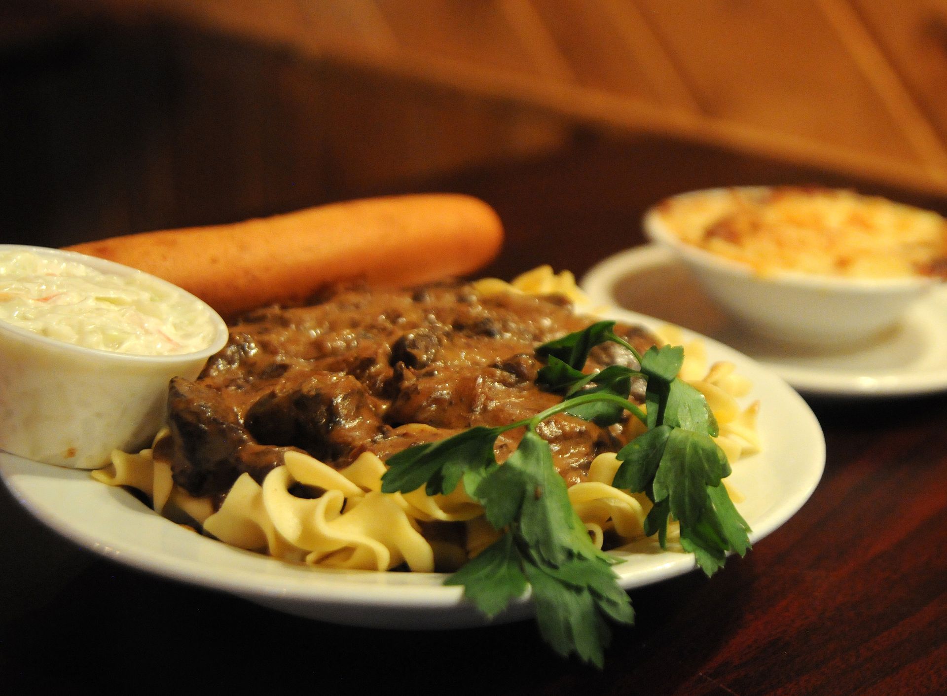 Plate of pasta with meat sauce, garnish, bread, and a side dish on a dark table