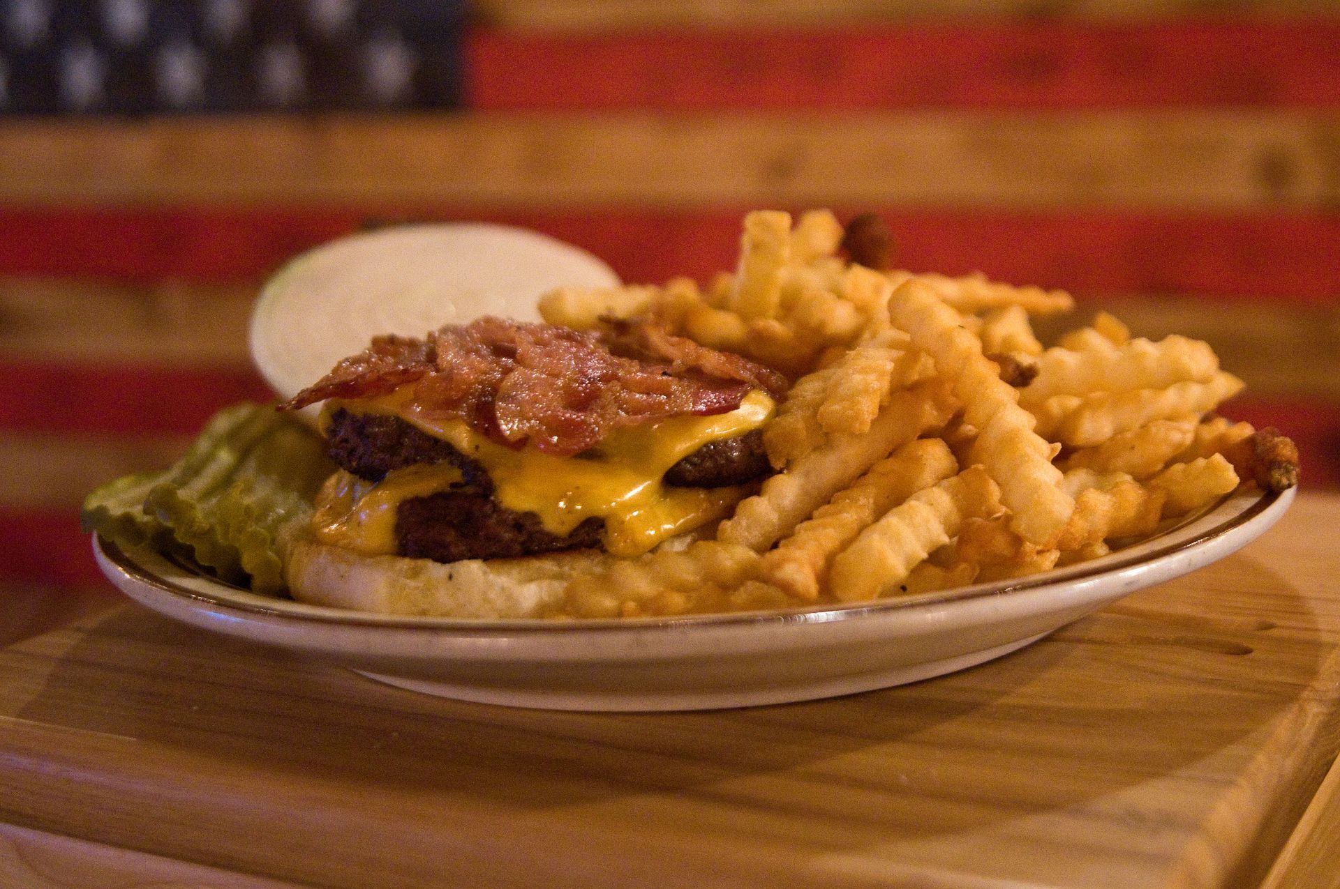 Plate of hamburger, crinkle-cut fries, and a pickle on a wooden table with a striped red background