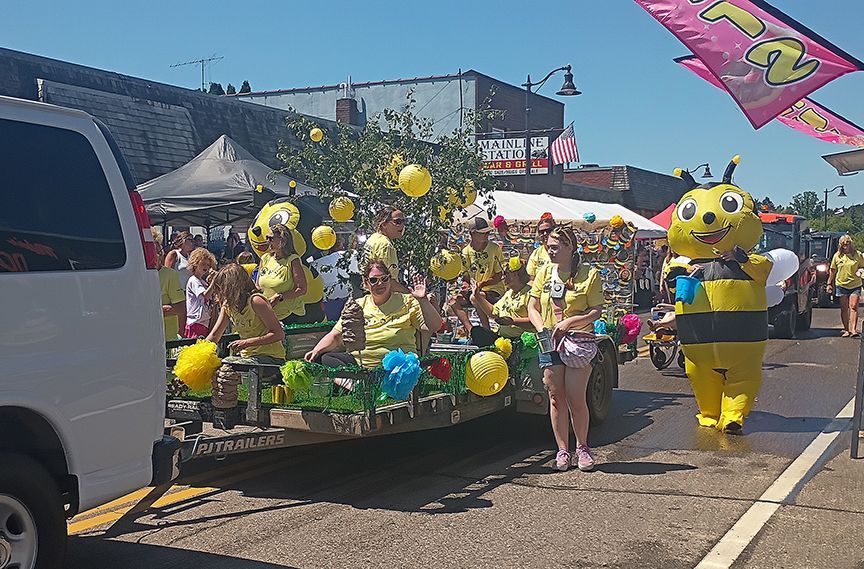 Decorated parade float with yellow balloons and costumes, with people standing beside it on a sunny street
